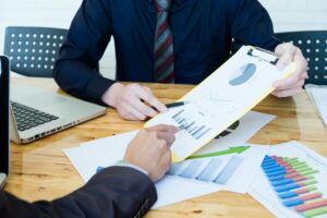 Canadian business professional negotiating a contract with suppliers, with financial charts in the background.